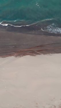 Sakin turkuaz dalgaların yavaşça kıyıya vurduğu ıssız bir sahilin yukarıdan görünüşü. Medya