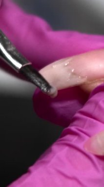 Manikür sırasında, eldiven teknisyeninin nazikçe kaldırma ve düzeltme için metal alet kullandığını gösteren tırnak temizliği. Medya