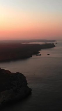 Sahil Koyu Uçurumlarının Üzerinde Yumuşak Pembe Günbatımı, Sakin Su, Uzak İsletler, Akşam Pususu ve Rüya Pastel Gökyüzü. Medya