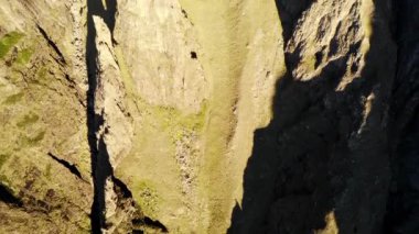 Dar geçitten geçen derin gölgeli, pürüzlü kaya yüzeyli ve çimenli havadan görünen dik uçurumlar. Medya