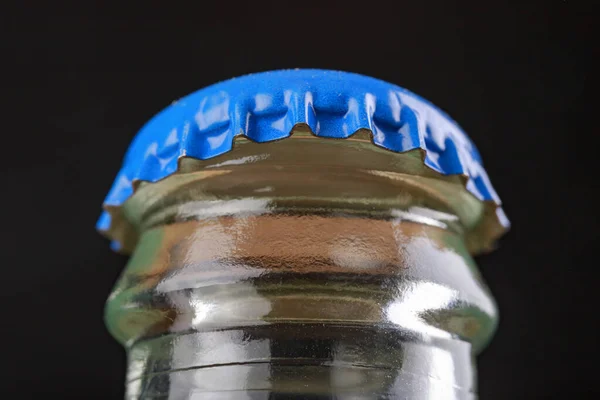 Metal cap on a glass bottle. An open bottle with a cold drink. Dark background.