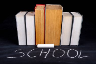 Okul sözcüğünün altında düzenlenmiş bir sıra kağıt kitap. Okul karatahtası ve kalın eğitim kitapları. Koyu arkaplan.
