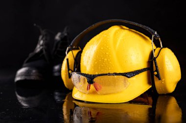 Bir prodüksiyon işçisi için ıslak giysi. Kaskta ve gözlüklerde yağmur damlası var. Koyu arkaplan.