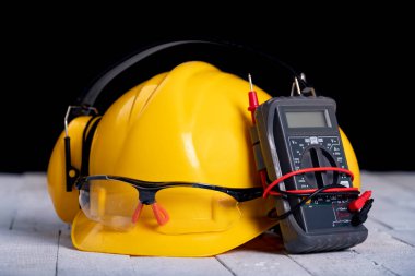 Tezgahın üzerinde bir kask ve koruyucu gözlük. Atölyedeki elektrik aksesuarları. Koyu arkaplan.