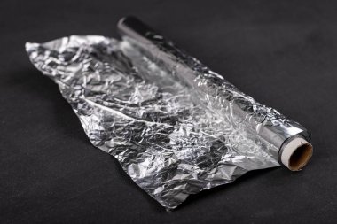 Karton silindirde alüminyum folyo yarası. Yiyecek depolamak için kullanılan malzeme. Koyu arkaplan.