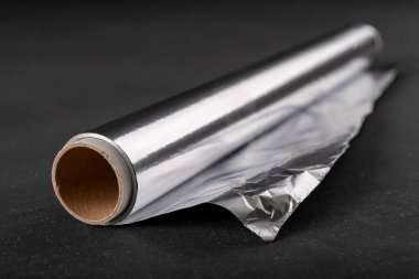 Karton silindirde alüminyum folyo yarası. Yiyecek depolamak için kullanılan malzeme. Koyu arkaplan.