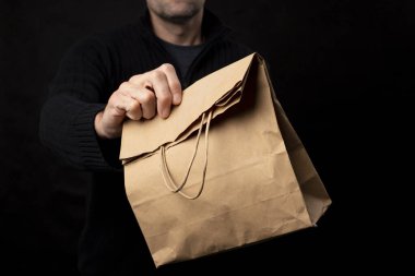 Bir kurye tarafından tutulan kağıt torba. Malların teslimatı ve eve teslimatı. Siyah arkaplan.