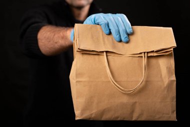 Bir kurye tarafından tutulan kağıt torba. Malların teslimatı ve eve teslimatı. Siyah arkaplan.