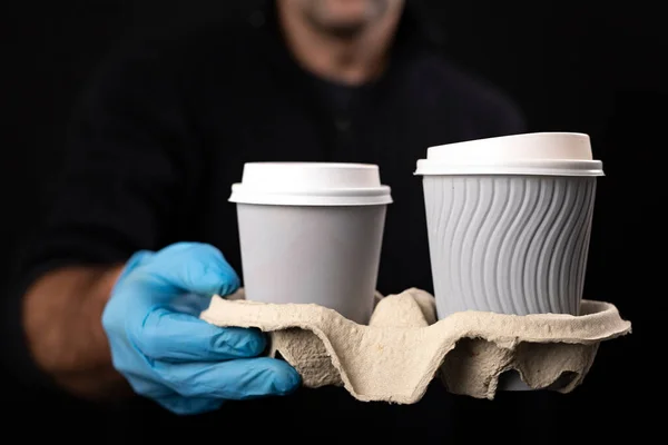 A set of hot drinks held by a courier. Delivery of goods ordered with home delivery. Dark background.