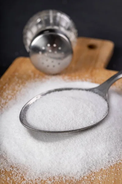 Metal spoon and spilled salt. A flavor enhancer added to dishes in home cooking. Dark background.