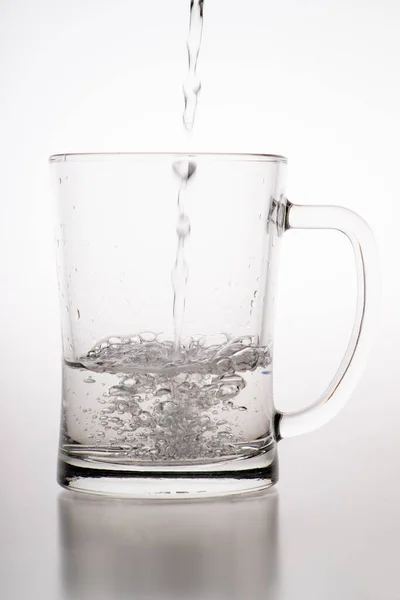 Pouring water into a mug. Glass container for weak carbonated alcohol. Light background.