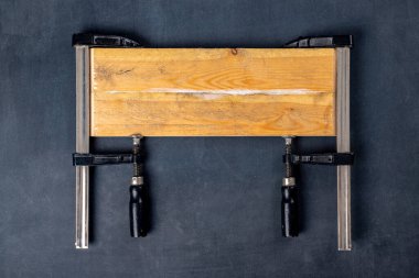 Ahşap parçalarını marangozluk yapıştırıcısıyla yapıştırmak. Marangozluk kıskaçları. Koyu arkaplan.