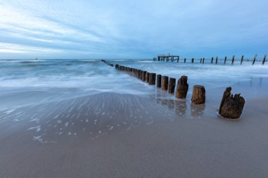 Köpüklü deniz suyu kumlu sahile dökülüyor. Deniz dalgası ahşap bir dalgaya çarpıyor. Sonbahar mevsimi.