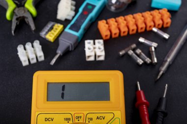 Tezgahtaki elektrik ölçümleri için bir metre. Elektrik teçhizatı onarımı ve kurulumu için aksesuarlar. Koyu arkaplan.