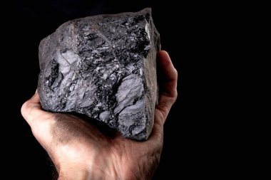 Kirli bir erkek elinin üzerinde duran kahverengi bir kömür yığını. Tek kişilik evleri ısıtmak için kullanılan malzeme. Koyu arkaplan.