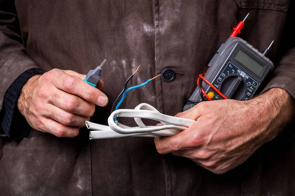 Electrician holding electrical accessories in his hands. Work in the electrical workshop. Dark background.
