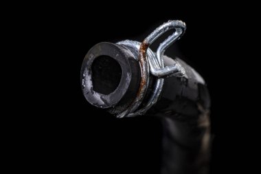 Metal kıskacı olan ıslak siyah bir hortum. Su ve kanalizasyon sistemlerini yenileyen tesisatçılar için aksesuarlar ve yedek parçalar. Siyah arkaplan.