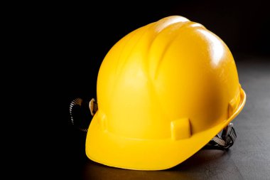 Koyu renkli bir masada sarı iş kaskı. İnşaat işçileri için koruyucu aksesuarlar. Koyu arkaplan.