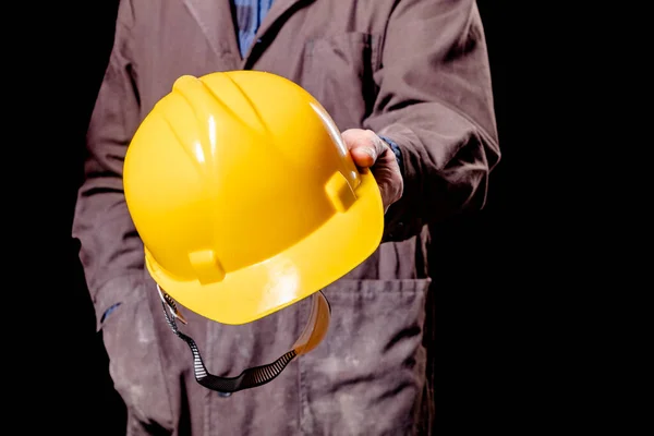 A production worker holding a yellow hard hat. Protective clothing in the workplace. Dark background.