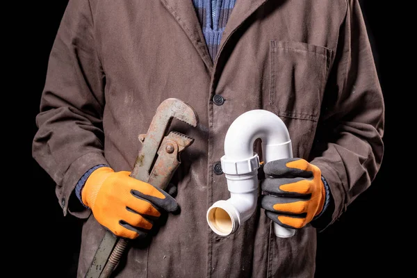 Plumber holding an adjustable wrench and a siphon to the wash basin. Worker repairing the hydraulic system. Dark background.