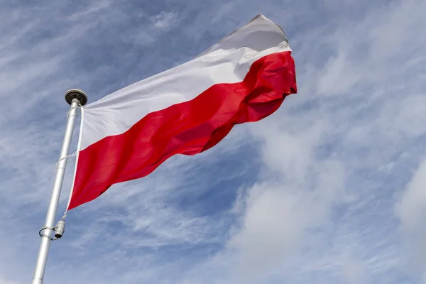Polish flag on a background of the cloudy sky. National symbol of Poland on the mast. Summer season.