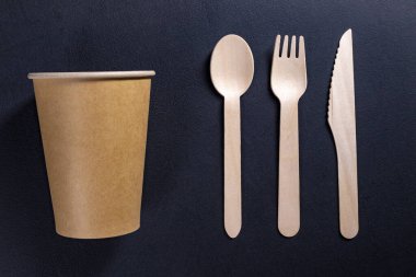 Tek kullanımlık ahşap çatal bıçak takımı ve karton kaplar. Açık havada yemek için aksesuarlar. Koyu arkaplan.