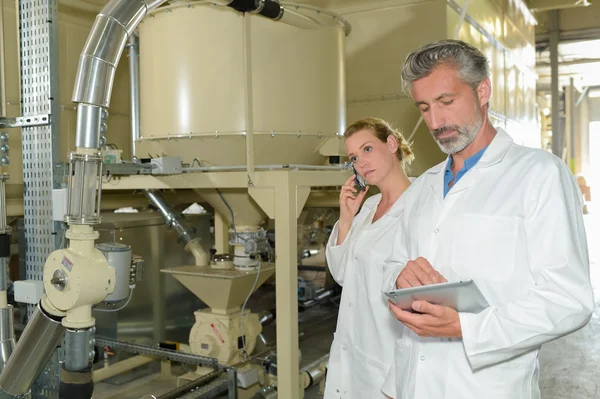 Hombre sujetando portapapeles, mujer en la celda en la fábrica — Foto de Stock