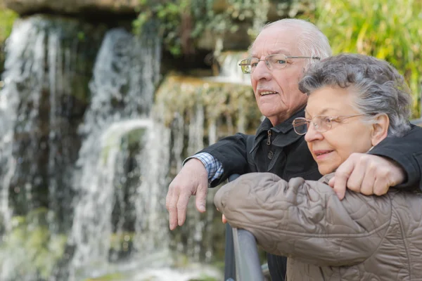 Elderly couple next to a waterfalls — Stock Photo, Image