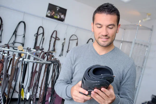 Hombre sosteniendo espinilleras en una tienda ecuestre — Foto de Stock