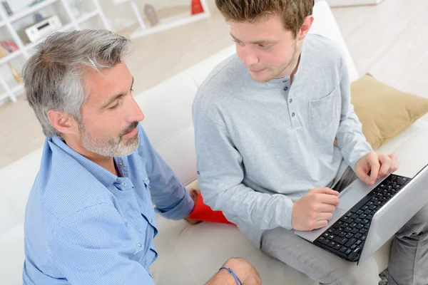 Young man using laptop, older man looking on — Stock Photo, Image