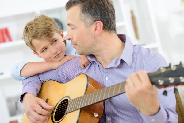 Mężczyzna gra na gitarze, dziecko, opierając się na jego ramieniu — Zdjęcie stockowe