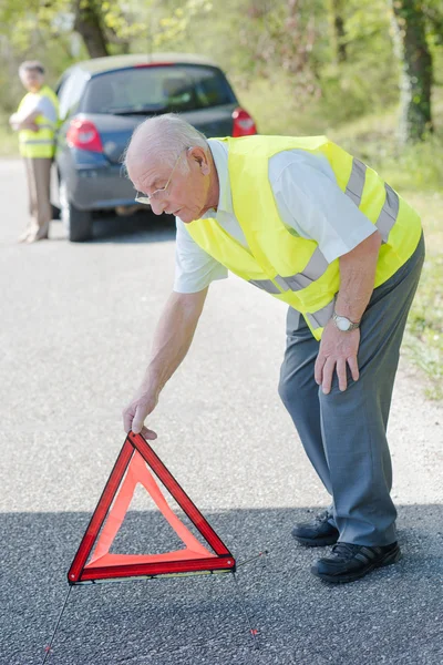 Coppia anziana guasto in auto, l'uomo mettendo triangolo di avvertimento rosso sulla strada — Foto Stock