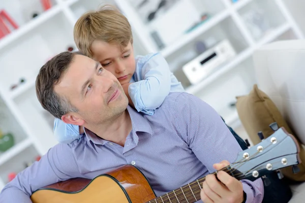 Man playing guitar, boy leaning on his shoulders — Stock Photo, Image