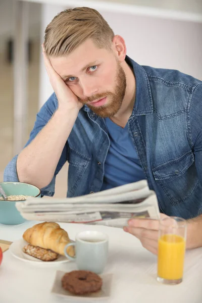 Znudzony Człowiek Czytający Gazetę Przy Stole Śniadaniowym — Zdjęcie stockowe