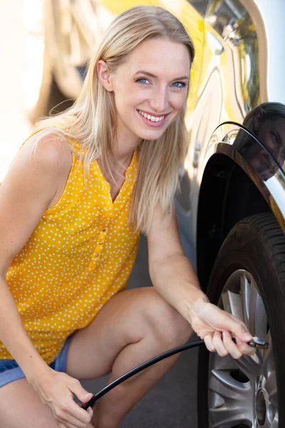 那位年轻妇女给她的汽车轮胎增加了空气 — 图库照片