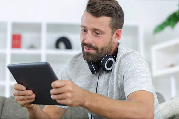 男人坐在沙发上 带耳机 使用数码平板电脑 — 图库照片
