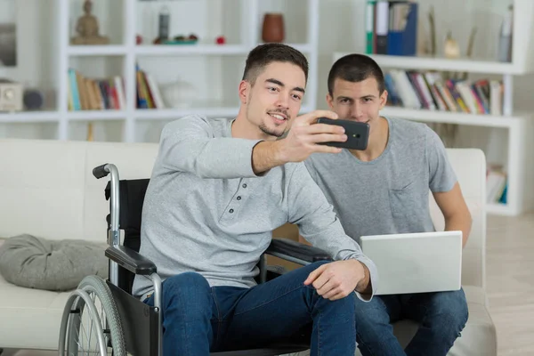 Δύο Νεαροί Άντρες Στο Σπίτι Βγάζουν Selfie Ένας Αναπηρική Καρέκλα — Φωτογραφία Αρχείου