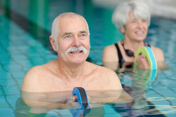 高齢の夫婦が浮き輪を持ってプールで運動をし — ストック写真