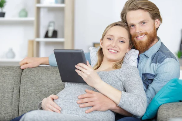美しい若い妊娠中のカップルとタブレットコンピュータがソファに座って — ストック写真