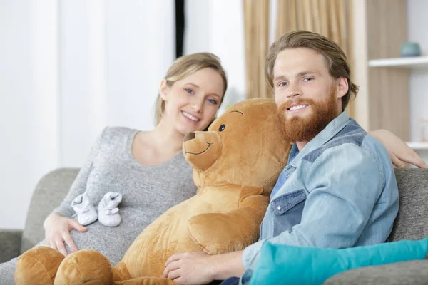 期待のカップルとソファの上の大きなテディ — ストック写真