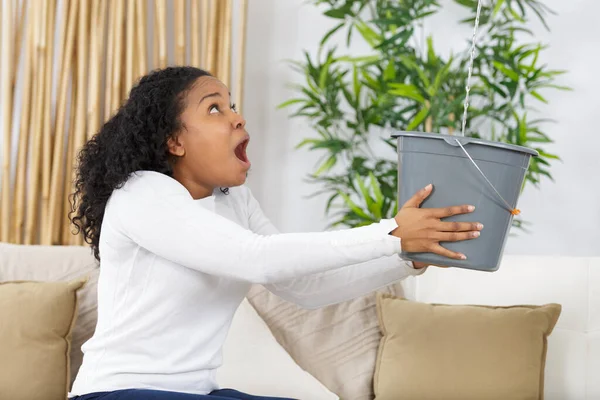 frustrated female client holding pot while water leaking from roof