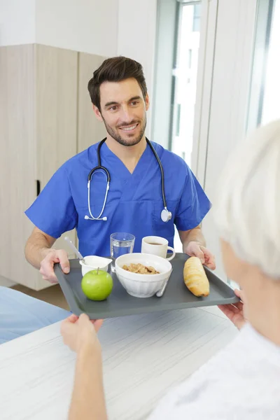 Mężczyzna Pielęgniarka Obsługujące Jedzenie Dla Senior Kobieta Pacjent Klinice — Zdjęcie stockowe