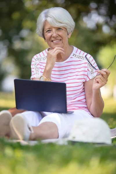活跃的老年妇女坐在草地上 手持笔记本电脑 — 图库照片
