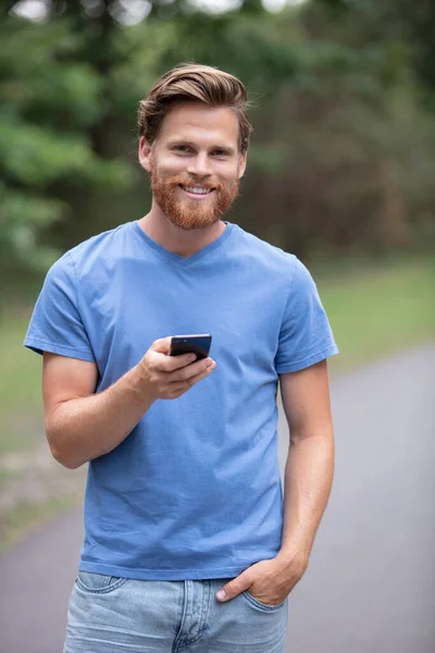 快乐的嬉皮士男人拿着电话在秋天的公园里散步 — 图库照片