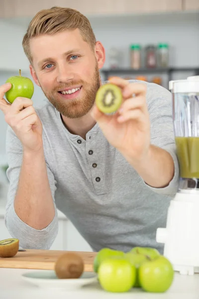 happy man making juice or smoothie in kitchen