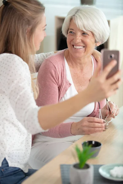 年长的母亲坐在沙发上 大女儿拿着智能手机 — 图库照片