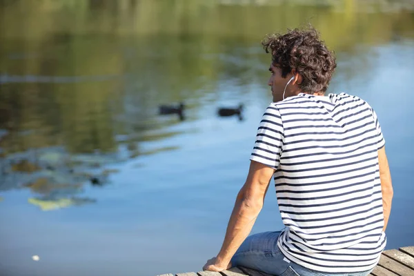 Joven Sentado Cerca Del Lago Escuchando Música —  Fotos de Stock