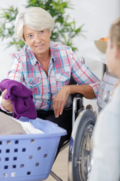 Elderly Woman Reading Book While Home Helper Irons Laundry — Stock Photo, Image