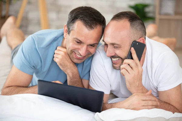 ゲイのカップルはラップトップを見て携帯電話を使って — ストック写真