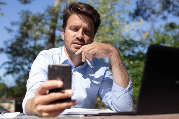 Adam Dışarıda Masa Başında Çalışırken Akıllı Telefona Bakıyor — Stok fotoğraf